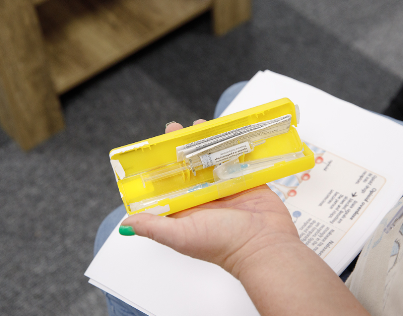 Close up of a hand holding a yellow naloxone injection kit