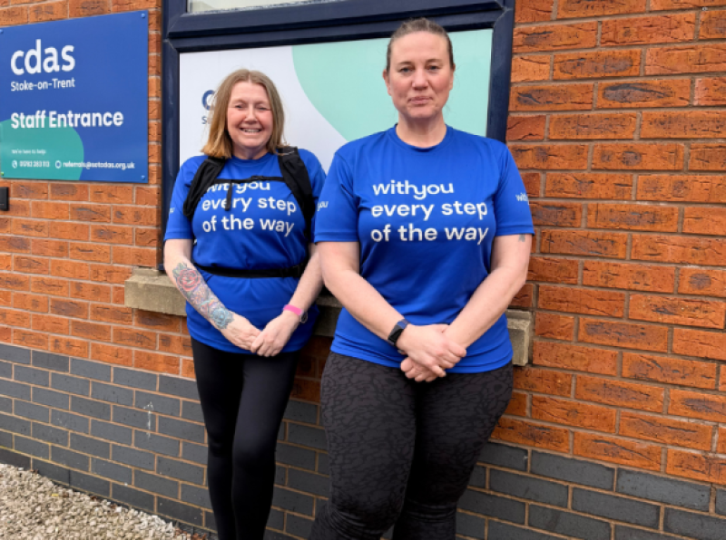 Jenny Douglas and Mandy Jones stand outside the CDAS building wearing blue "WithYou every step of the way" t-shirts. A CDAS staff entrance sign is visible on the brick wall behind them.