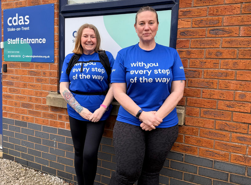 Jenny Douglas and Mandy Jones stand outside the CDAS building wearing blue "WithYou every step of the way" t-shirts. A CDAS staff entrance sign is visible on the brick wall behind them.