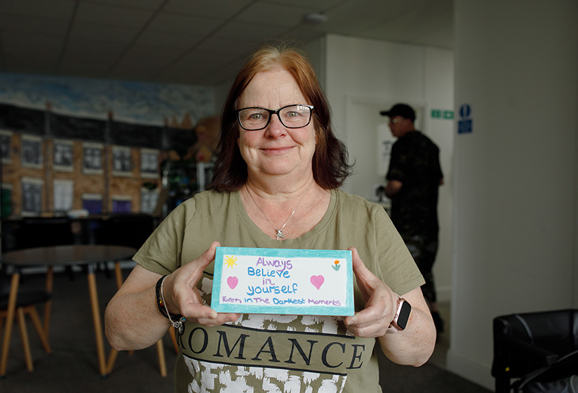 Woman smiling and holding a handmade sign that says 'Always believe in yourself'